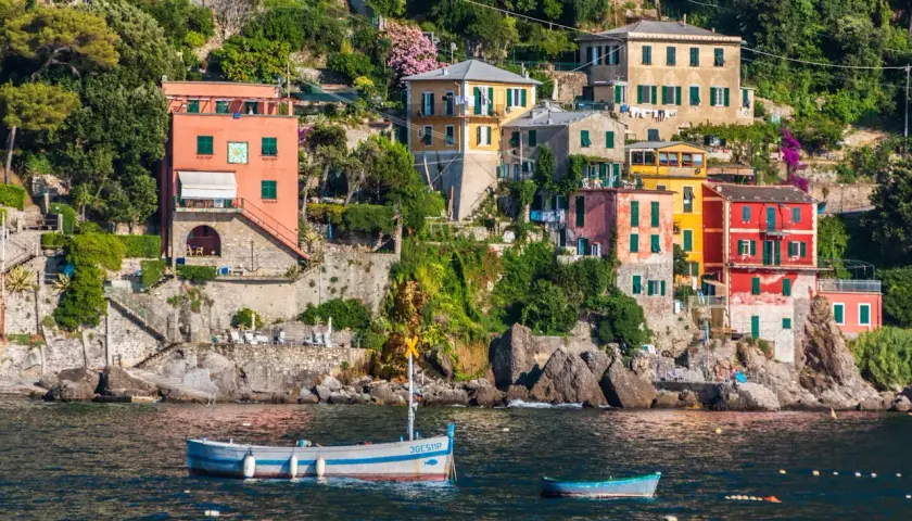 Des maisons colorées s'accrochent à la falaise sur la **riviera italienne où aller**. Des bateaux flottent paisiblement dans l'eau bleue.