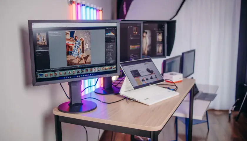 Profesjonalny monitor do obróbki zdjęć, z programem Lightroom, pokazuje zdjęcie kobiety w sukience. Obok laptop i inne monitory.