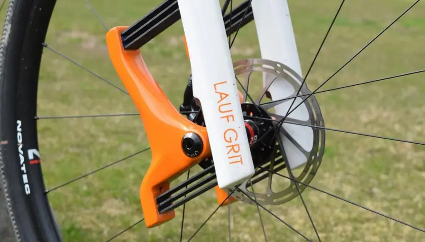 Close-up of a bright orange and white Lauf Grit fork on a bicycle wheel, ready for adventure.