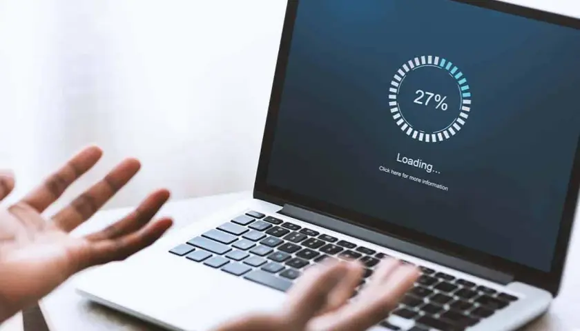 Verzweifelte Person schaut auf Laptop, auf dem "Loading... 27%" steht. Windows startet nach Update nicht mehr.