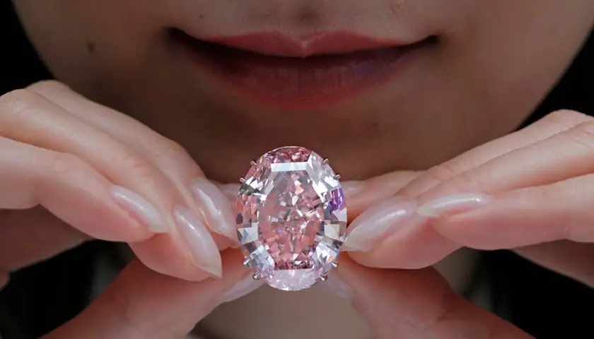 Hände halten einen rosafarbenen Diamanten. Welche Diamanten Farbe ist die teuerste? Rosa Diamanten sind extrem selten und wertvoll.