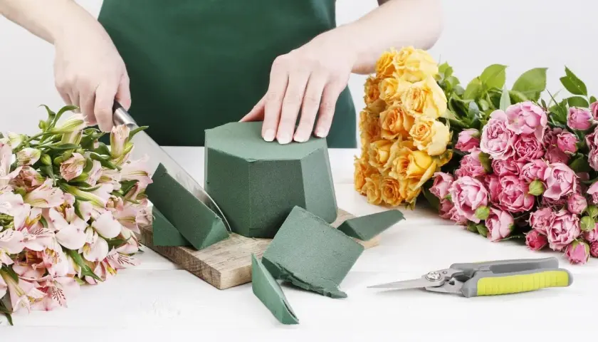 Préparation d'un bouquet : on coupe la mousse pour piquer des fleurs, entourée de roses jaunes et roses.