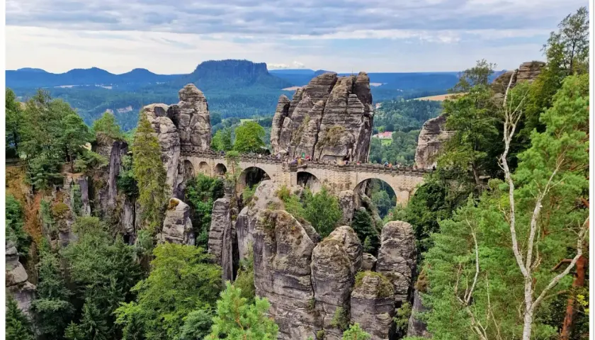 Kamienny most Bastei w saksońskiej Szwajcarii, łączący skalne baszty. Widok na malowniczy krajobraz z lasami i wzgórzami.