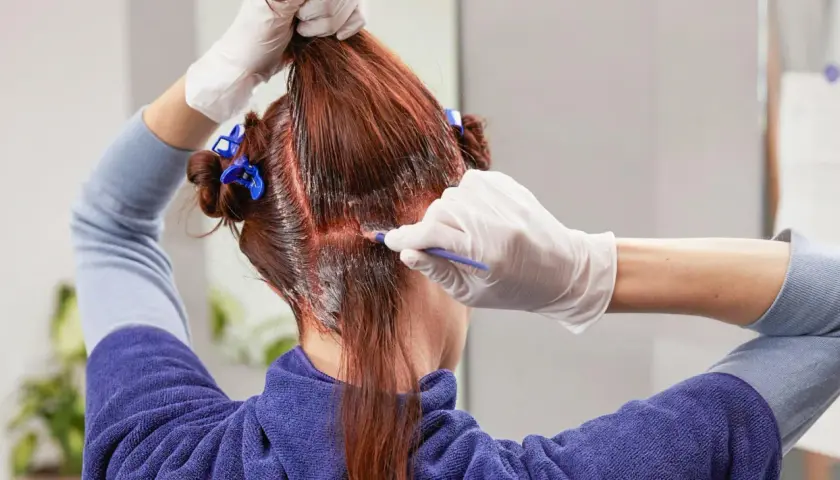 Persona se tiñe el pelo en casa, aplicando tinte con un pincel.