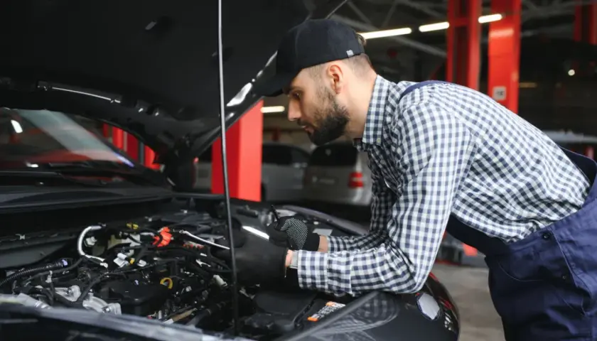 Mechanik w czapce i kratowanej koszuli bada silnik samochodu. Wygląda na to, że próbuje rozwiązać problem, który mógł wpędzić auto w **tryb awaryjny**.