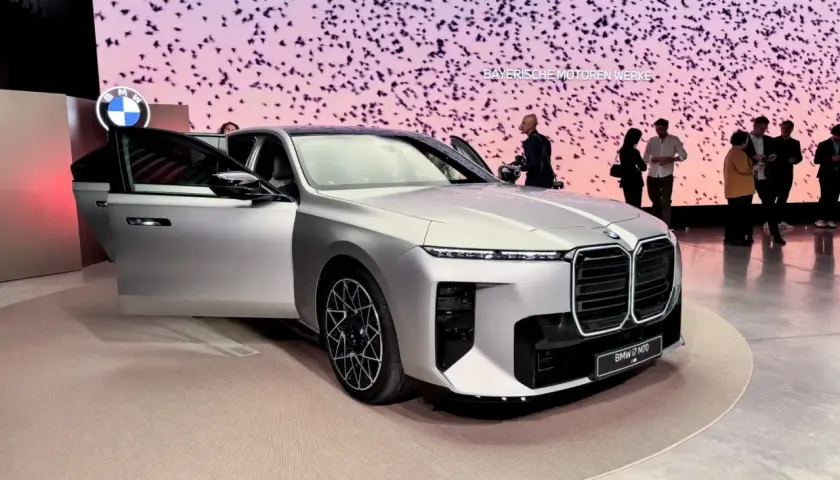 Elegancki, srebrny BMW i7 M70 G10 z otwartymi drzwiami na wystawie. Tło zdobią stylizowane ptaki i logo BMW.