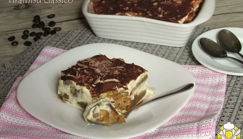 Una fetta di tiramisù classico, con savoiardi inzuppati nel caffè e crema al mascarpone, spolverato di cacao e scaglie di cioccolato. La ricetta del tiramisù è un classico intramontabile.