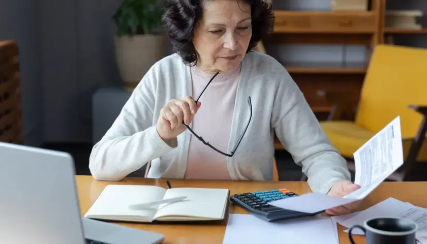 Kobieta analizuje dokumenty, zastanawiając się, czy odprawa emerytalna jest opodatkowana. Na biurku laptop, kalkulator i notatnik.