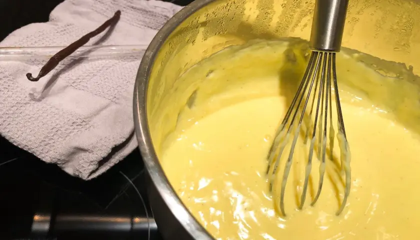 Crema pasticcera senza latte in preparazione, con bacca di vaniglia e frusta.