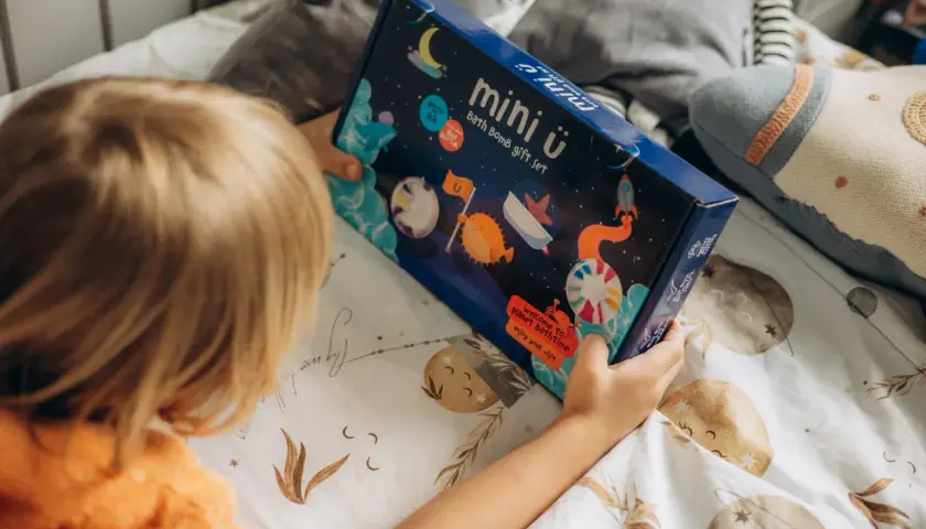 Dziecko trzyma pudełko z zestawem do kąpieli "mini ü". Na opakowaniu są kosmiczne motywy, które podpowiadają, jak używać kuli do kąpieli dla wspaniałej zabawy.