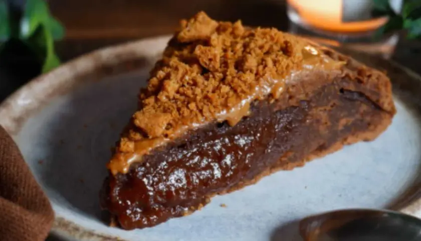 Une part de gâteau speculoos, riche et gourmande, garnie de miettes de biscuits et d'une sauce caramel.