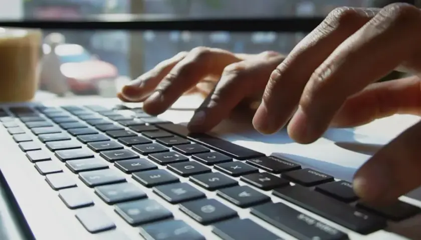 Mains sur un clavier d'ordinateur portable, une tasse de café à proximité. L'utilisateur interagit avec un chatbot helpdesk pour obtenir de l'aide.