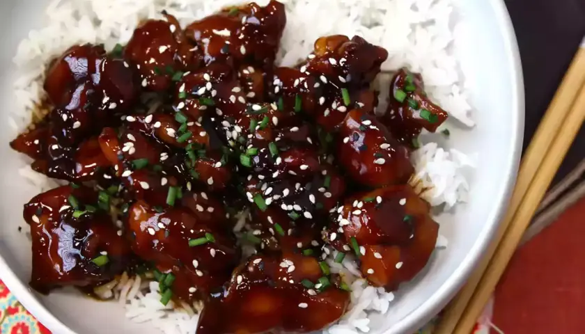 En skål med fluffigt ris toppad med glaserad teriyaki kyckling, strödd med sesamfrön och gräslök.