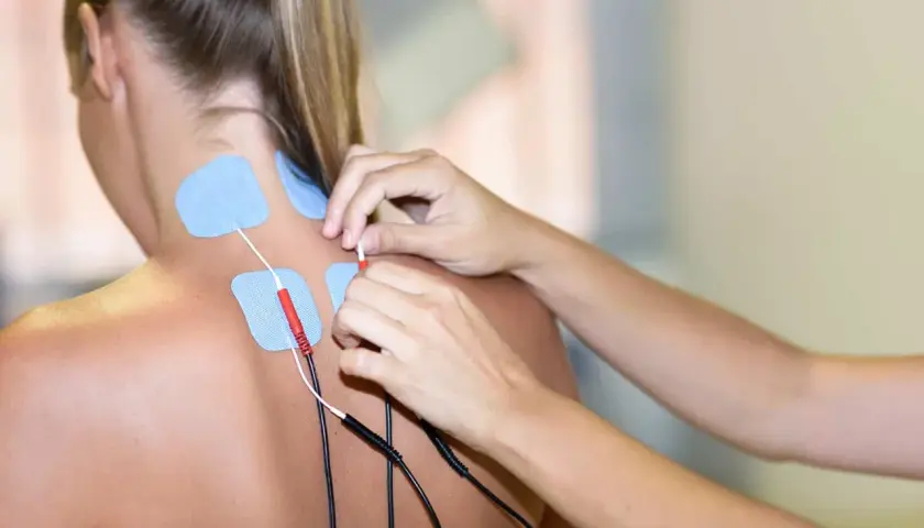 Fizjoterapeuta zakłada elektrody na kark pacjentki, przygotowując ją do zabiegu prądów interferencyjnych.