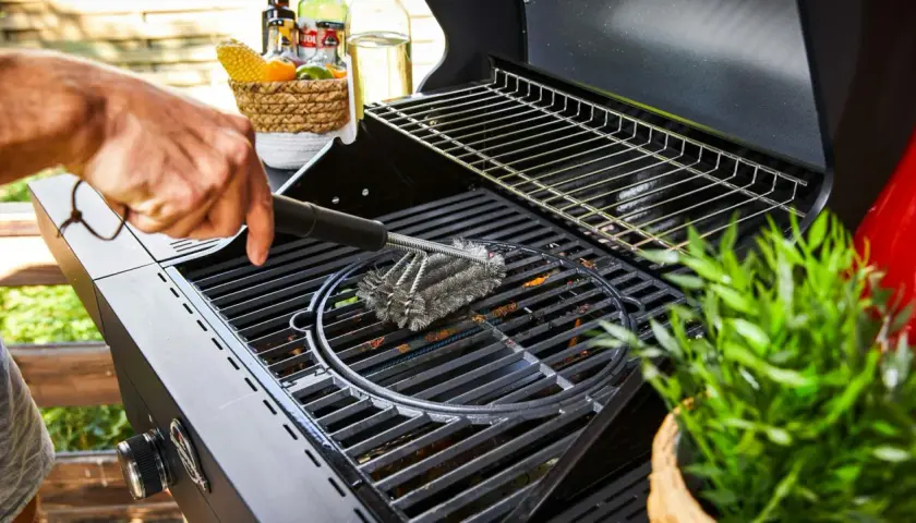 Main d'homme utilisant une brosse métallique pour nettoyer la plaque du barbecue.