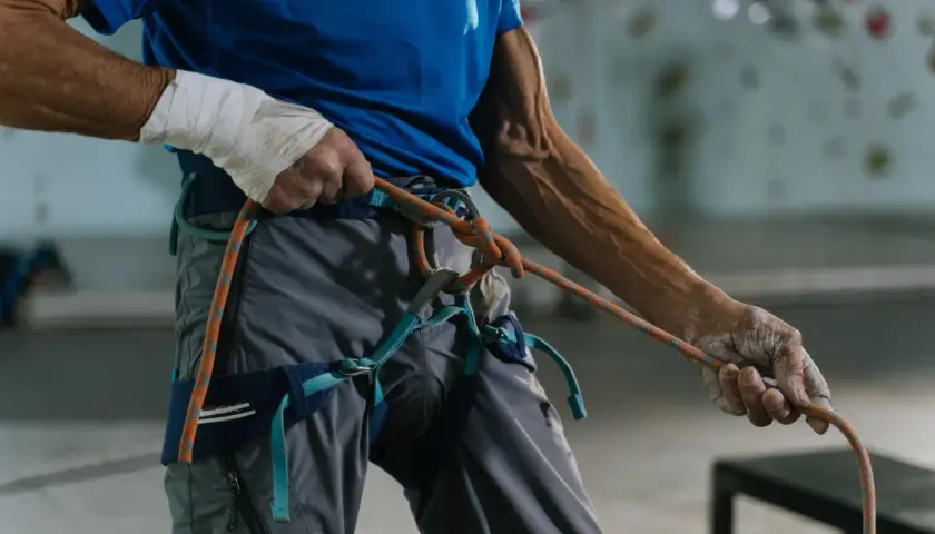 Mann mit bandagierter Hand prüft den klettergurt richtiger sitz und das Seil.