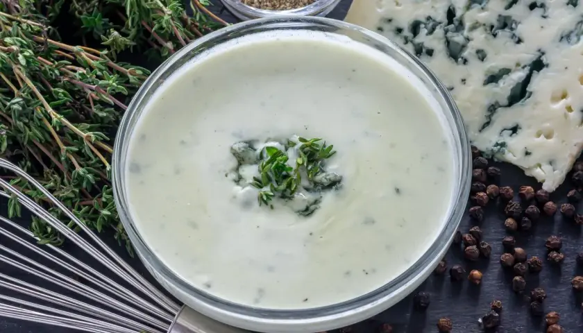 Crema suave con trozos de queso azul y tomillo fresco, lista para convertirse en una deliciosa salsa roquefort.