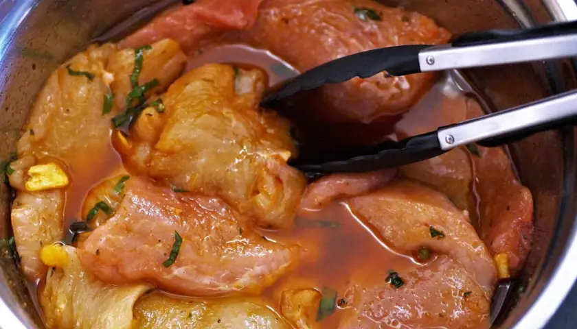 Morceaux de porc marinés dans une sauce rouge, prêts à être cuits. Une araignée de porc se cache dans la marinade.