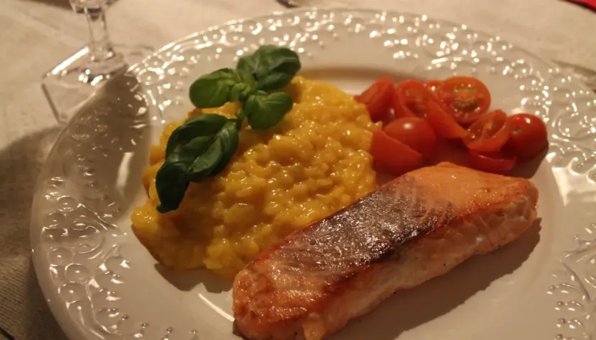 En härlig saffransrisotto med lax, garnerad med basilika och serverad med körsbärstomater. En festlig rätt!