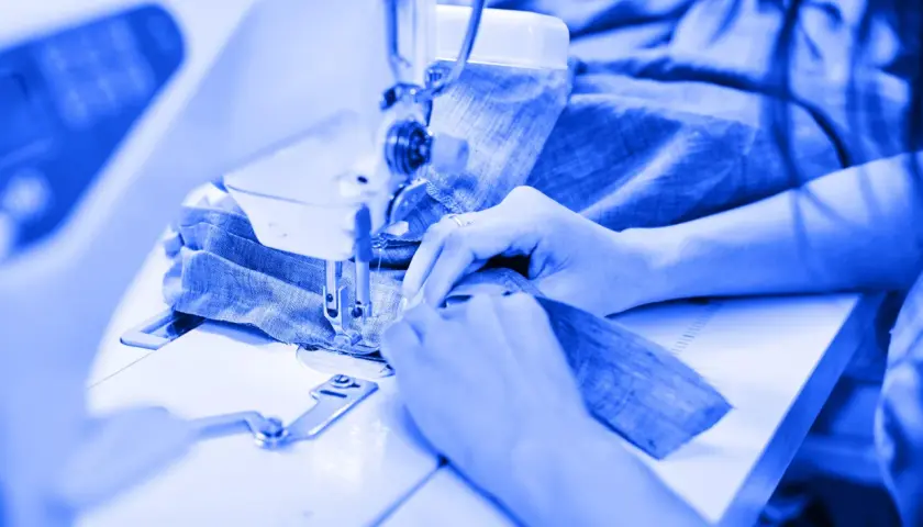 Mains guidant du tissu bleu sous une machine à coudre, un aperçu de l'industrie du vêtement en pleine action.