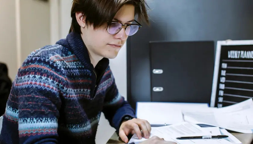 A young man with glasses studies documents, working towards his online public administration certificate.