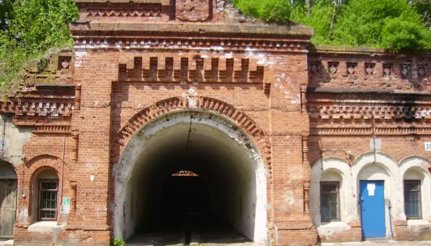 Wejście do tunelu w ceglanej twierdzy Osowiec. Zarośnięte zielenią mury i łukowate przejście.
