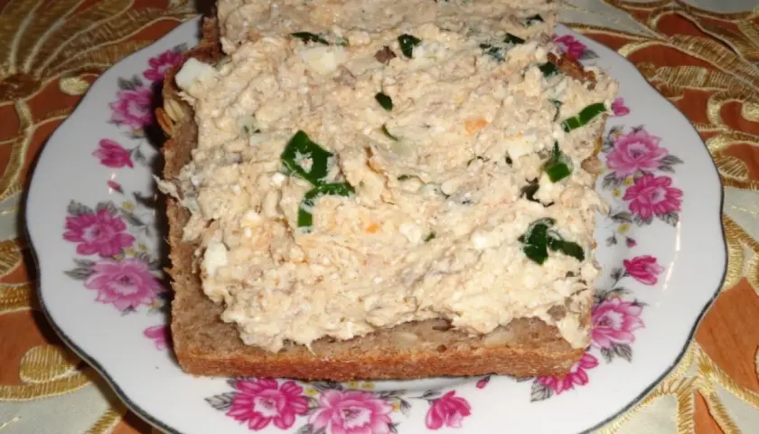 Pyszna pasta z makreli i twarogu z zieloną cebulką na ciemnym chlebie, podana na talerzu z różami.
