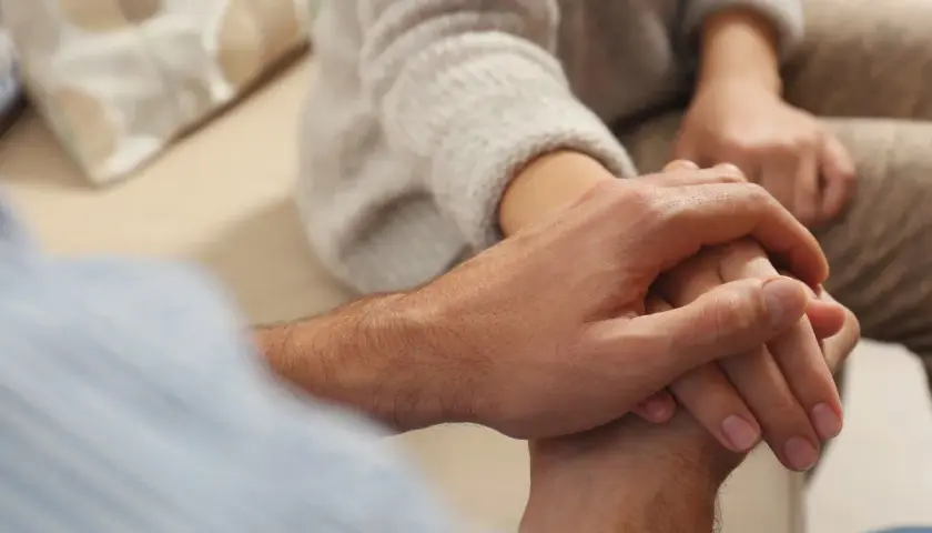 Dłoń mężczyzny obejmuje dłoń kobiety, pokazując, jak pocieszyć dziewczynę w trudnych chwilach.