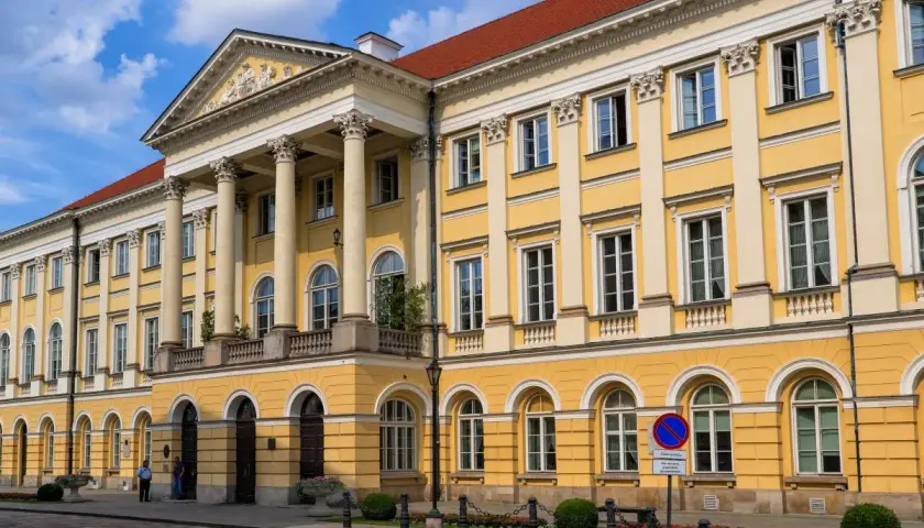 Majestatyczny żółty budynek z kolumnami, jeden z wielu uniwersytetów w Polsce, z czerwonym dachem i błękitnym niebem.