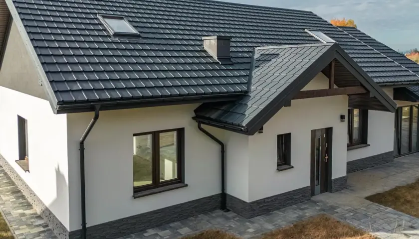 Nowoczesny dom z ciemnym dachem i solidnymi systemami rynnowymi, chroniącymi jego fundamenty.
