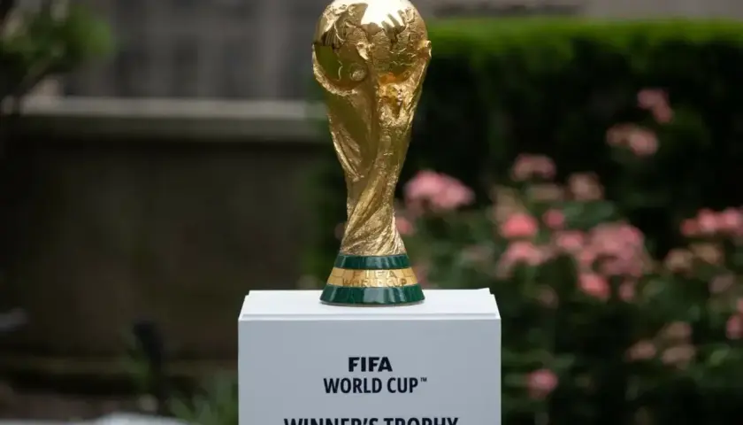 Złote trofeum FIFA World Cup, symbol zwycięstwa w mistrzostwach świata, lśni na tle zieleni i różowych kwiatów.