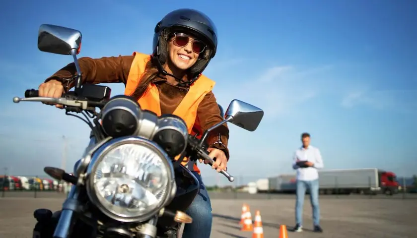 Uśmiechnięta kursantka na motorze, w kasku i kamizelce, uczy się jeździć. Zastanawia się, jakie prawo jazdy na motor 1000 będzie potrzebne.