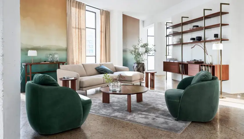 Salon moderne avec canapé beige, fauteuils verts et étagères en bois, ambiance mid century.