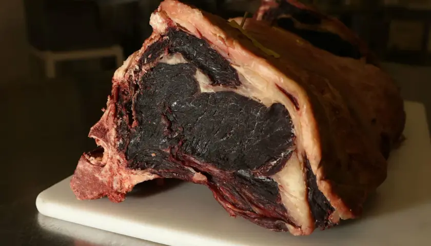 Gros morceau de viande maturée, prêt pour la cuisson. Sa couleur foncée et sa texture fibreuse promettent une saveur intense.