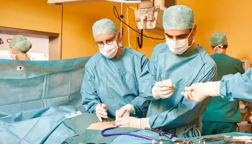 Chirurgen führen eine Hernien-OP mit Netz durch. Ein Team arbeitet konzentriert, um Komplikationen zu vermeiden.