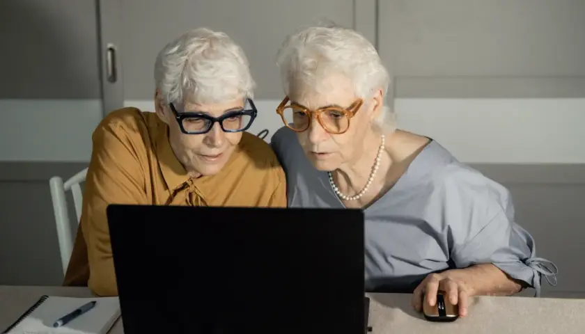 Dwie starsze kobiety w okularach patrzą na ekran laptopa.