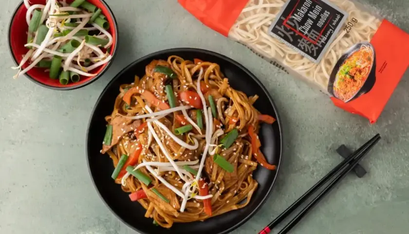 Talerz makaronu chow mein z warzywami i kiełkami fasoli, obok paczka makaronu i miseczka kiełków.