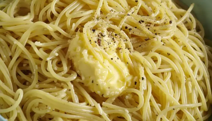 Spaghetti fumanti con burro fuso e pepe nero macinato, pronti per la cacio e pepe ricetta originale romana.