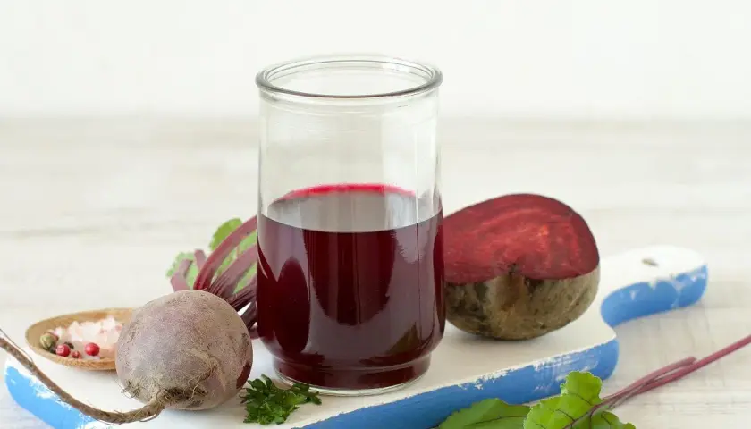 Szklanka z intensywnym, rubinowym sokiem z kiszonych buraków, obok świeże buraki i przyprawy. Zdrowie w płynie!