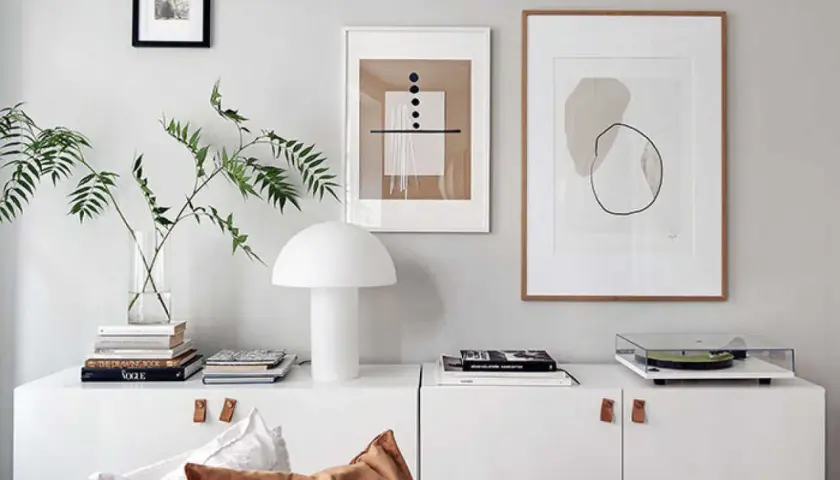 En vit skåp med en lampa, böcker, en skivspelare och tre tavlor utan ramar på väggen.