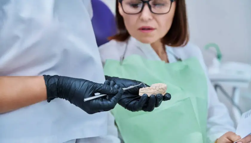 Dentysta pokazuje pacjentce model szczęki, omawiając problem połknięcia plomby amalgamatowej.
