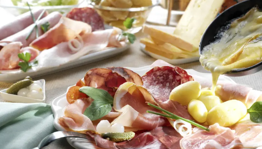 Assiette de charcuterie et pommes de terre, avec du fromage fondu versé dessus. Un délice pour un repas raclette.