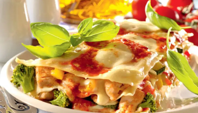 Pyszne lasagne z kurczakiem, brokułami i pomidorami, udekorowane świeżą bazylią.