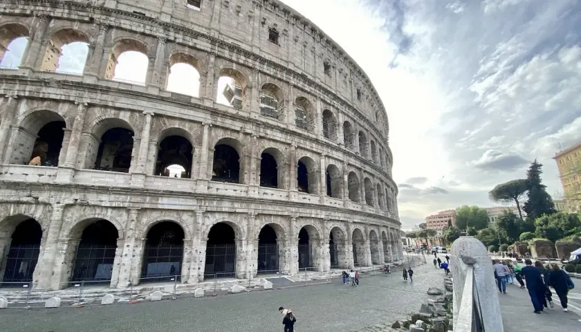 Vue extérieure du Colisée, monument emblématique de Rome. Des touristes profitent de leur visite colisée sous un ciel nuageux.