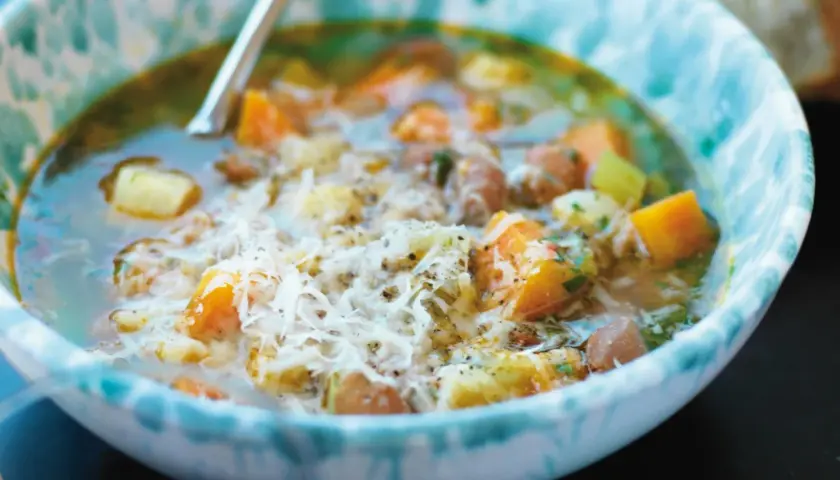 En närbild av en skål med en mustig gryta, kanske ett molokhia recept, med bitar av grönsaker och kött, toppad med riven ost.