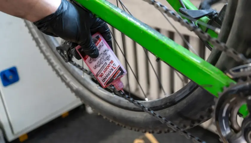 Ręka w czarnej rękawiczce aplikuje różowy olej do łańcucha zielonego polskiego roweru.