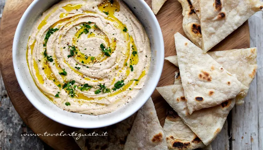 Cremoso hummus di fagioli, condito con olio d'oliva e prezzemolo, servito con pane pita tostato.