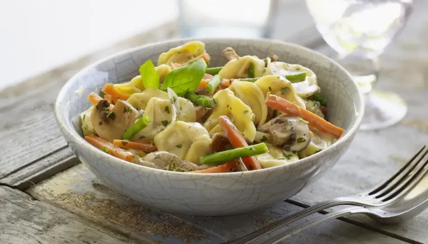 Tortellini con champiñones, zanahoria y espárragos en una cremosa salsa para pastel de verduras.
