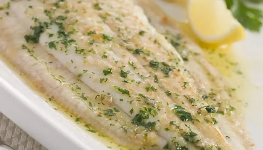 Sogliola alla mugnaia succulenta, cosparsa di prezzemolo fresco e servita con spicchi di limone.