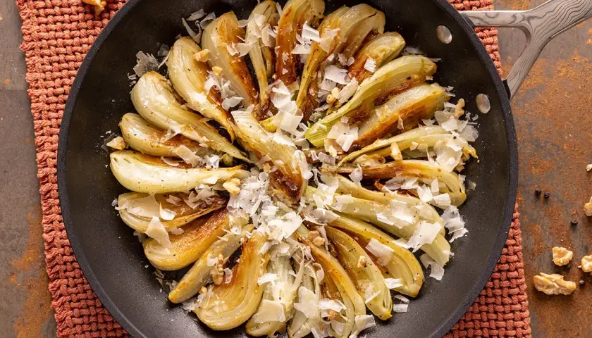 Finoçchi gratinati in padella, dorati e saporiti, guarniti con scaglie di formaggio e noci croccanti.